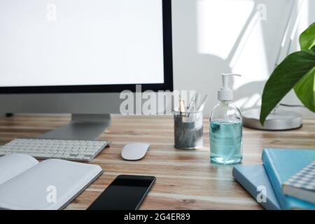 Pump bottle with hand sanitizer on desk of person, next to computer, planner, and smartpphone Stock Photo