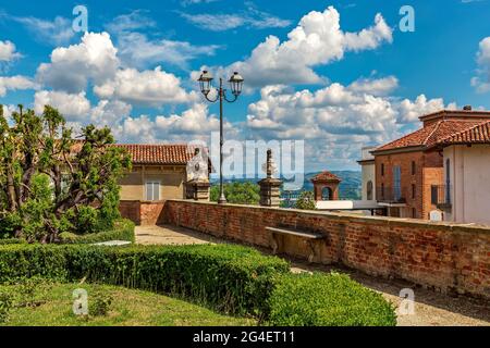Green bushes in the park and typical houses under beautiful blue sky with white clouds in small town of Govone in Piedmont, Northern Italy. Stock Photo