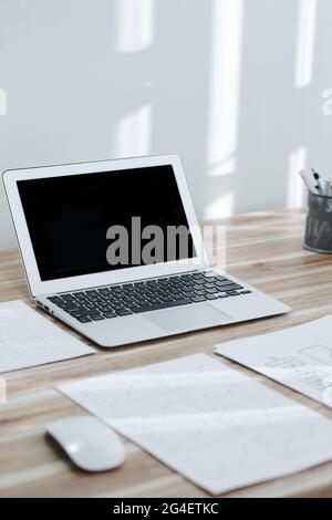 Opened laptop with black empty screen and various reports on office desk Stock Photo