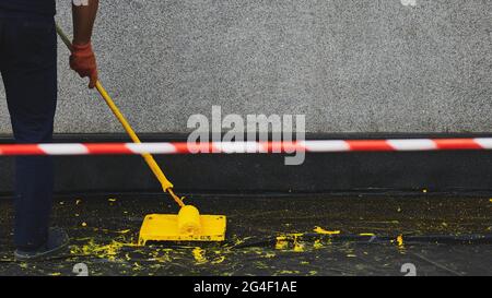 Signal tape beside painting the building. Man painting a wall in yellow colour. Paint roller in a paint tray near a grey wall. Black plastic cover on Stock Photo