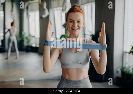 Portrait of young sporty redhead woman in sportswear with resistance rubber band Stock Photo