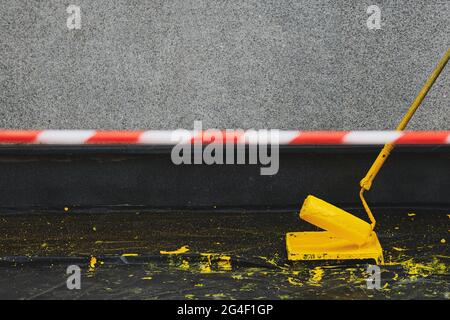 Signal tape beside painting the building. Paint roller in a paint tray near a grey wall. Painting the wall in yellow colour. Black plastic cover on th Stock Photo