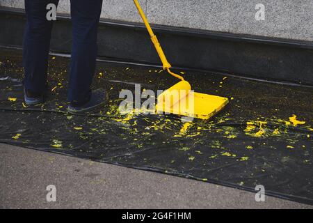 Man painting a wall in yellow colour. Paint roller in a paint tray near a grey wall. Black plastic cover on the ground. Stock Photo