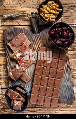 Dark chocolate bar with hazelnuts, peanuts, cranberries and freeze dried raspberries on a wooden board. wooden background. Top view Stock Photo