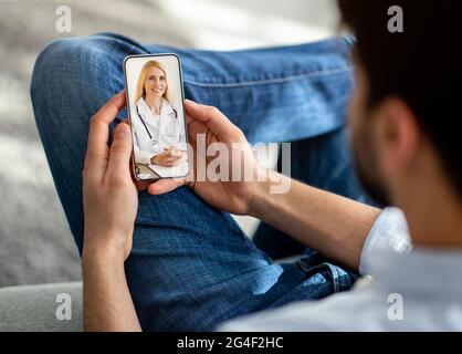 Unrecognizable man using cellphone at home, talking to doctor Stock Photo