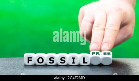 Hand turns dice and changes the expression "fossil" to "fossil free". Stock Photo