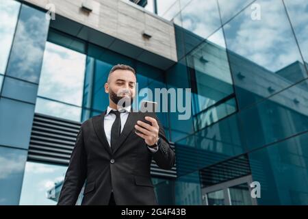 Business lifestyle concept. Handsome businessman using smartphone, standing against office building, copy space Stock Photo