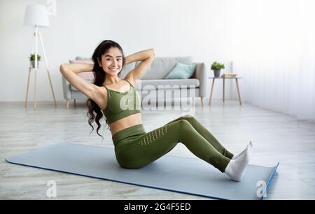 Athletic Indian woman doing exercises on yoga mat, strengthening her abs muscles at home. Domestic sports Stock Photo