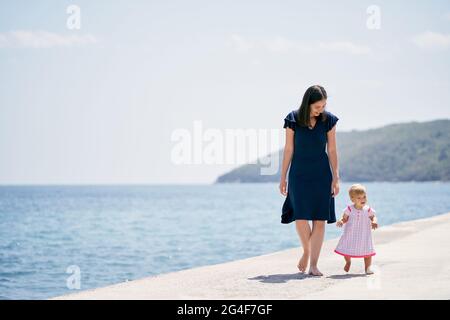 Smiling mom with little girl walking along the breakwater Stock Photo