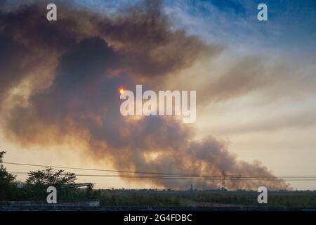 Smoke coming out of factories in the horizon, air pollution is spreading like clouds and covering the setting sun. Shot at rural village of WB, India. Stock Photo