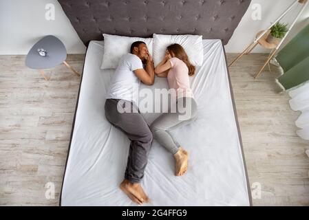 Full length of affectionate multiracial couple sleeping together on bed, facing each other, top view Stock Photo