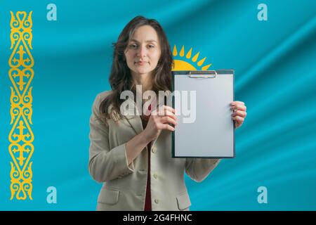 Study in Kazakhstan Beautiful woman holding a sheet of paper in her hands. Girl on the background of the flag of Kazakhstan. Stock Photo