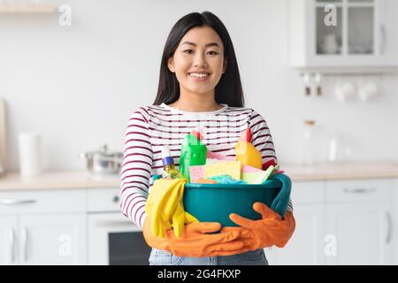 Happy asian woman with cleaning tools standing at kitchen Stock Photo