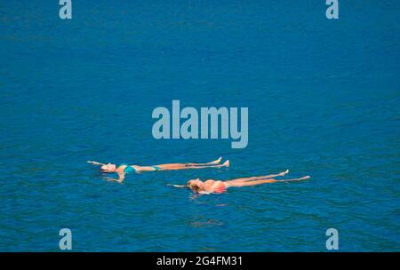 Kalkan, Turkey, 2020. Two young ladie floating  in the sea near to moored charter yachts in a sheltered part of Kalkan bay in Turkey;  located on the Stock Photo