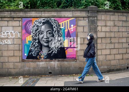 21st June, 2021. Edinburgh, Scotland, UK. Woman wearing headphones walking by a portrait of Dr Anne-Marie Imafidon MBE by artist Shona Hardie. Stock Photo