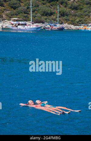 Kalkan, Turkey, 2020. Two young ladies floating in the sea near to moored charter yachts in a sheltered part of Kalkan bay in Turkey;  located on the Stock Photo
