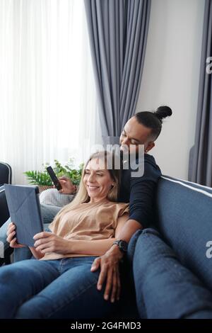 Happy couple relaxing on sofa and watching entertaining show on tablet computer Stock Photo