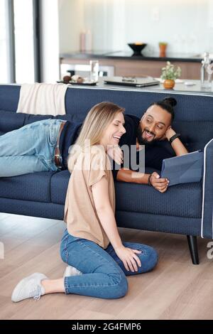 Man lying on sofa and showing funny video on tablet computer to his laughing girlfriend Stock Photo