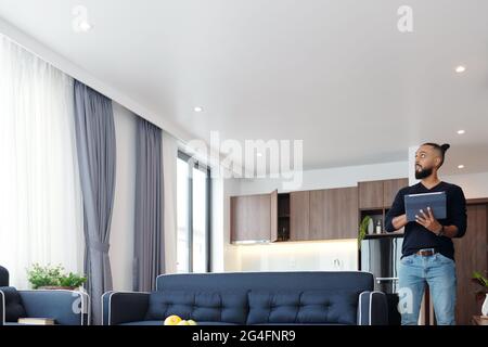 Bearded man using application on tablet computer when controlling light and temperature in his apartment Stock Photo