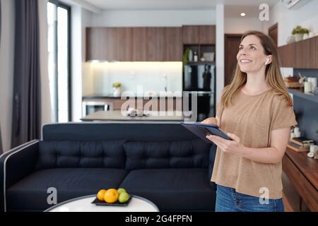 Joyful young woman with digital tablet using smart home app to control air conditioner temperature Stock Photo