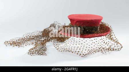. Small hat of stitched red rips silk with flat sphere and light upstanding edge, decorated with brown grosgrain and brown voile. Model: Loose ball and edge. The sphere, which tapered from top to bottom, consists of two parts with a seam around. The sphere is reinforced with horsehair, the edge with Laiton. In the edge a seam in the middle. Unlined. Brown Ripslint. Decoration: around the sphere a 3 cm wide ribbon of brown grosgrain, which is stretched on the right in a double flat bow. On the front a coarse mesh voile, a dependent strip of the same tulle at the back. Stock Photo