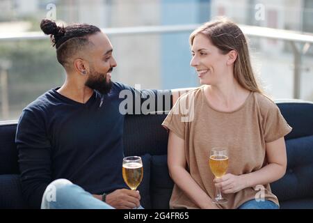 Smiling young man and woman drinking cold wine and talking at rooftop party Stock Photo