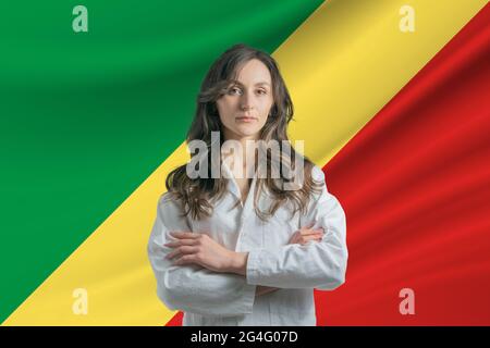 Medicine in Republic of the Congo Happy beautiful female doctor in medical coat standing with crossed arms against the background of the flag Stock Photo