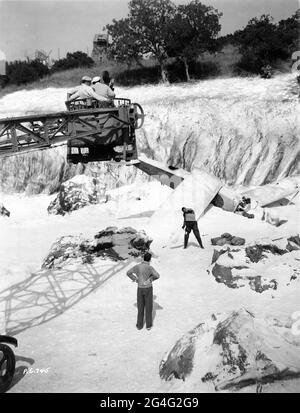 JOHN FORD directing RALPH BELLAMY with giant electric Camera Crane and Movie Crew above during filming of a plane crash scene in snow on the sunny Universal Studios Back Lot for AIR MAIL 1932 director JOHN FORD story Dale Van Every and Frank Wead screenplay Frank Wead cinematographer Karl Freund presenter Carl Laemmle Universal Pictures Stock Photo