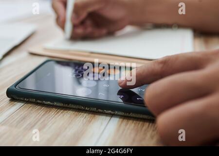 Close-up image of businesswoman using calculator application on smartphone and writing in planner Stock Photo