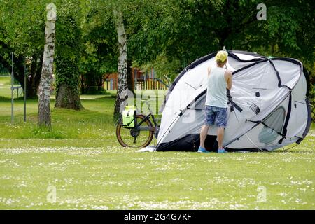 Kreuzlingen, Switzerland 05 20 2021: A man setting up a tent in a park. There is bike behind the tent. Copy space is on the foreground. Stock Photo