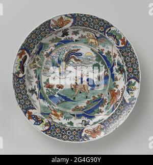 . Dish of Faience. Plychrome painted: on the flat inside a circle a rock landscape with a kilin and a bird. The four boxes placed around it have a corresponding decor. Edge decorated with braid in which six saved medallions with butterflies. Stock Photo