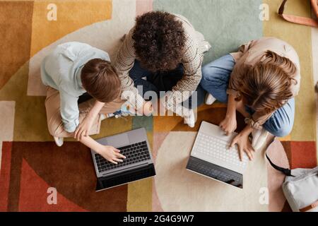 Top down view at group of three kids using computers while sitting on floor carpet Stock Photo