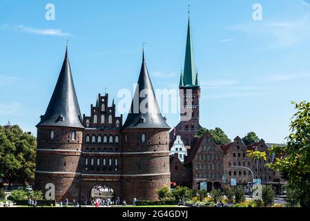 Facade of the Holsten Gate or Holstentor, medieval fortification and the St. Peter church with people around in Lübeck, Germany Stock Photo