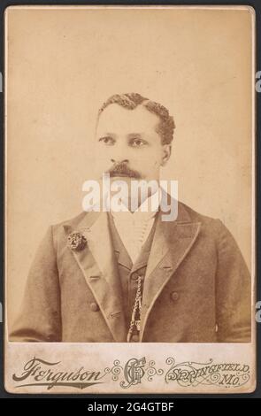 A black and white photograph of Tobe Brown.;Brown is pictured from the waist up. He has curly hair with a side part and a long mustache. He is wearing a white collared shirt, a vest, and a suit jacket. He has a metal chain on his vest and a flower lapel pin on the proper right side of his jacket.;There is a thin white border around 3/4 of the photograph. It is thicker on the bottom and there is black text below the image which reads [Ferguson] on the left, [GWF] in the center, and [SPRINGFIELD / MO.] on the right. The corners are a bit worn and there is slight discoloring on the back. A handwr Stock Photo