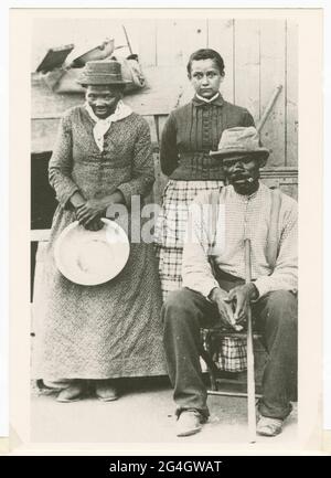 A black-and-white postcard featuring a photograph of Harriet Tubman, her husband Nelson Davis, and their adopted daughter Gertie. African-American anti-slavery activist Harriet Tubman (c1820-1913) was born into slavery in Maryland. She escaped in 1849, became a leading Abolitionist and was active as a 'conductor' in the Underground Railroad, the network which helped escaped slaves to reach safety. Tubman stands on the left holding a round pan. The postcard was sent to Mariline Wilkins in Philadelphia, PA from Sedalia Gaines in 1992. Stock Photo