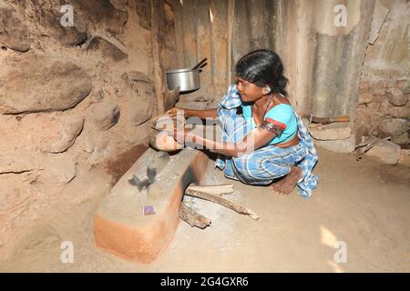 LANJIA SAORA TRIBE. Tribal woman making Ragi food using mud pot and traditional mud hearth in kitchen. Puttasingh village in Odisha, India