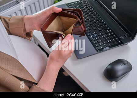 Pregnant woman with laptop in home office shows empty wallet without finances Stock Photo