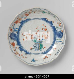 . Porcelain plate with scalloped edge, painted in underglaze blue with rocks, and on the glaze in blue, red, green, yellow and black with a pot with prunus on the mirror and two birds between prunus and bamboo. Around the mirror and along the edge a double underglazing blue line. On the back leaf refinters in underglaze blue. Some preen in the foot ring. Dirty in glazur cracks. Old label on the bottom with 'Collection Westendorp / 8'. Kakiemon style. Stock Photo