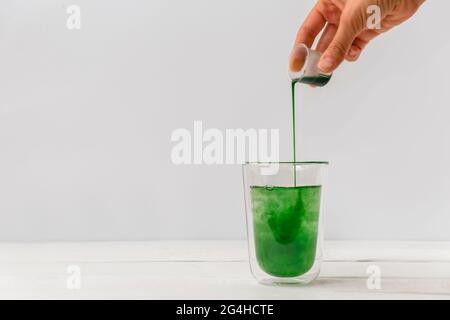 Woman hand pouring liquid chlorophyll in a glass cup. White background with space for text Stock Photo