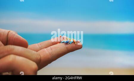 Close up side shot of microplastics on human fingers with blurred sea background. Creative concept of water pollution and global warming. Stock Photo