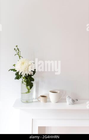 A large chrysanthemum in a glass vase, two fluted cups of coffee and ceramic bird figurines on the table. Office decoration. Stock Photo