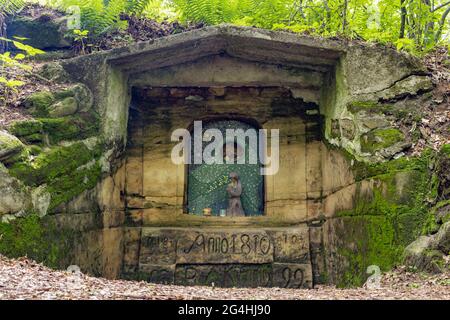 Chapel with a figure of the Virgin Mary holding Jesus Christ carved in stone wall in the forest, the 19th century, Czechia. Stock Photo