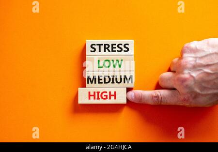 Low or high stress level symbol. Businessman chooses the wooden block with words high stress. Words stress low medium high. Beautiful orange backgroun Stock Photo