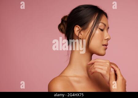 Young asian woman with beautiful skin. Beautiful female with her eyes closed against pink background. Stock Photo