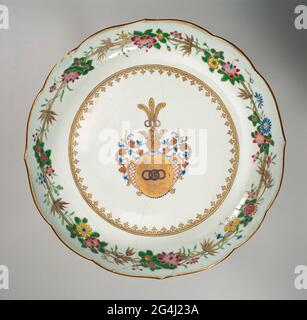 . Scale of porcelain with scalloped edge, painted on the glaze in blue, red, pink, green, yellow, black and gold. On the flat the coat of arms of the Zurmegede family in gold with three terraced rings. The helmet sign is a crown with three-switched rings and peacock feathers above. The cover comprises a cartouche with a diamond shaped pattern in the style of Louis XIV along with leaves and a row of pearls on either side. A Spearhead border on the wall. On the edge a decoration of flower drinks and bamboo. Plate has been broken. Weapon porcelain with email colors. Stock Photo