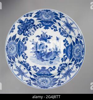 . Porcelain plate, painted in underglaze blue. On the flat a bird on a rock in blooming plants and a butterfly; The wall and edge alternately with foliage shell motifs including a mask with tendrils and a medallion with flower branches including a Ruyi motif; On the wall and edge the arm of the Pelgrom family surrounded by Acanthus leaves; The helmet sign, a Chinese man, rising from a lotus. The back with three valuables (books, artimisia leaf, music stone). Marked on the bottom with two fish in a double circle. Weapon porcelain in blue and white. Stock Photo