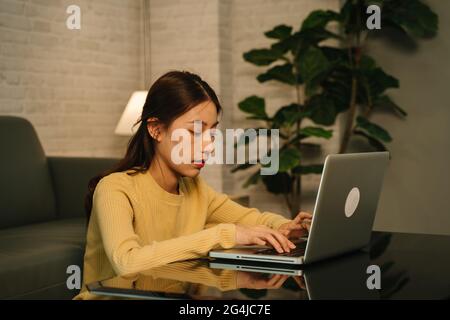 Workaholic and tired young Asian businesswoman working overtime on laptop till late night completing client project at home Stock Photo