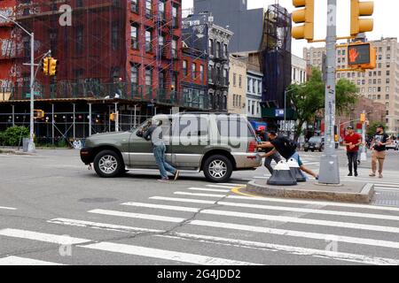 People pushing a disabled car across an intersection in New York City. Stock Photo