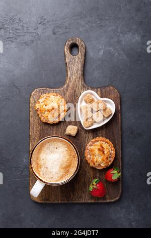 Ceramic mug with coffee, tasty cakes and strawberries on dark stone background. Top view - Image Stock Photo