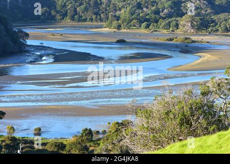 Tidal river meandering through estuary among mudflats exposed at low tide. Stock Photo